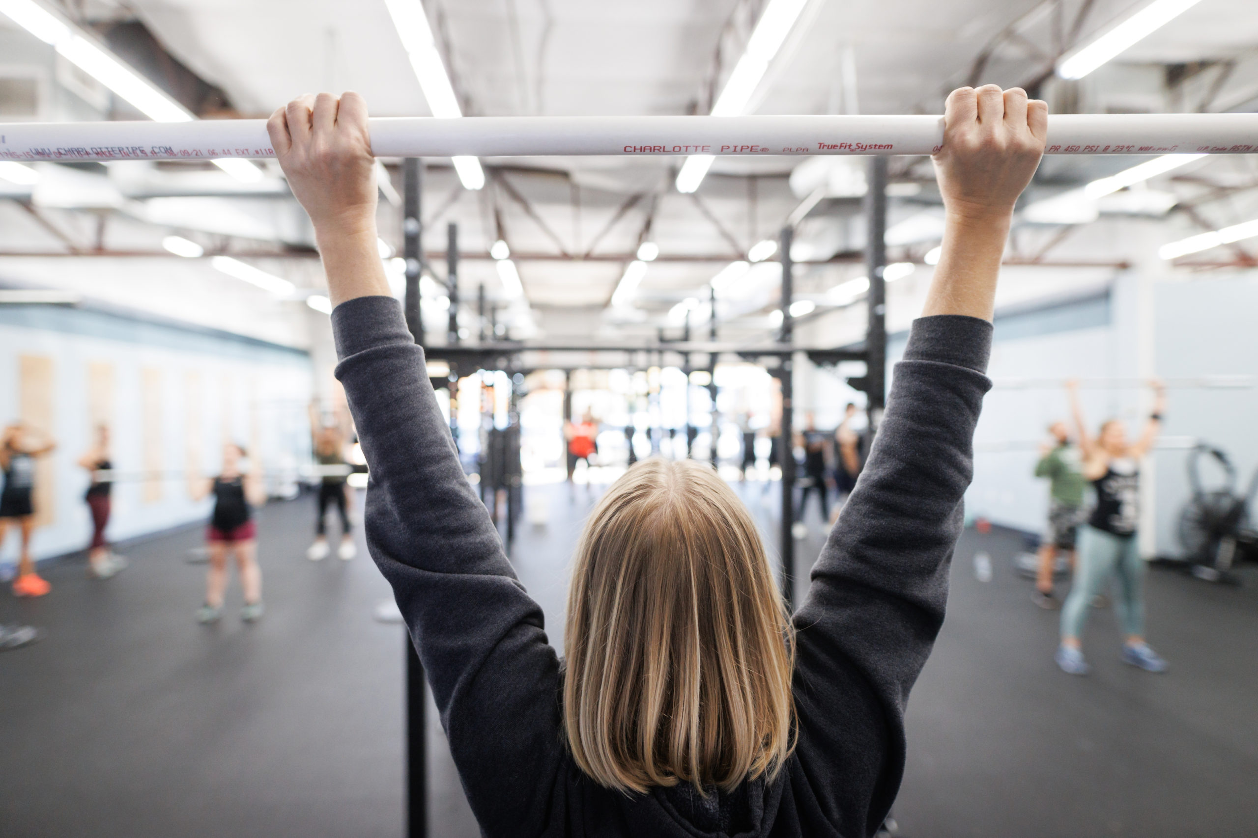 An athlete facing away from the camera holds a PVC pipe overhead. 