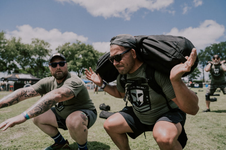 One athlete doing an air squat and another doing a back squat with a ruck during Manion WOD