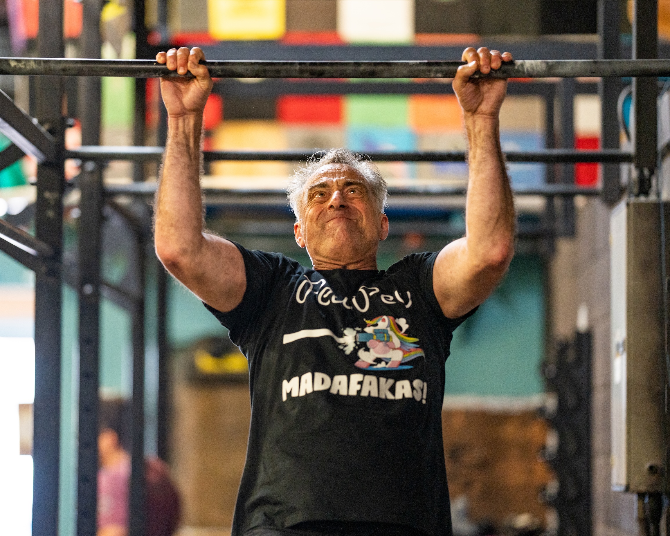 An older man grimaces with effort, hanging from the pull-up bar.